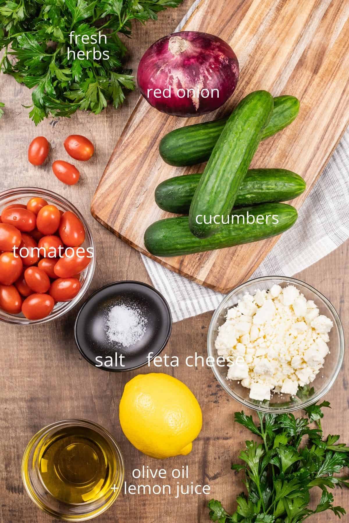 ingredients for cucumber salad on a cutting board and in various glass bowls on the wood table