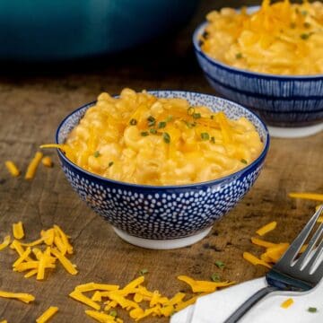 close up of two bowls of extra cheesy Mac and cheese with extra cheese sprinkled around the bowls