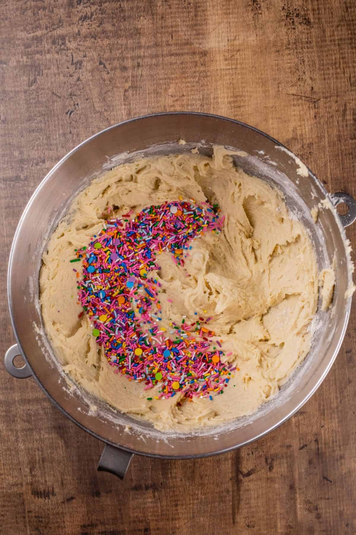 adding sprinkles to the finished cookie dough in a silver mixing bowl