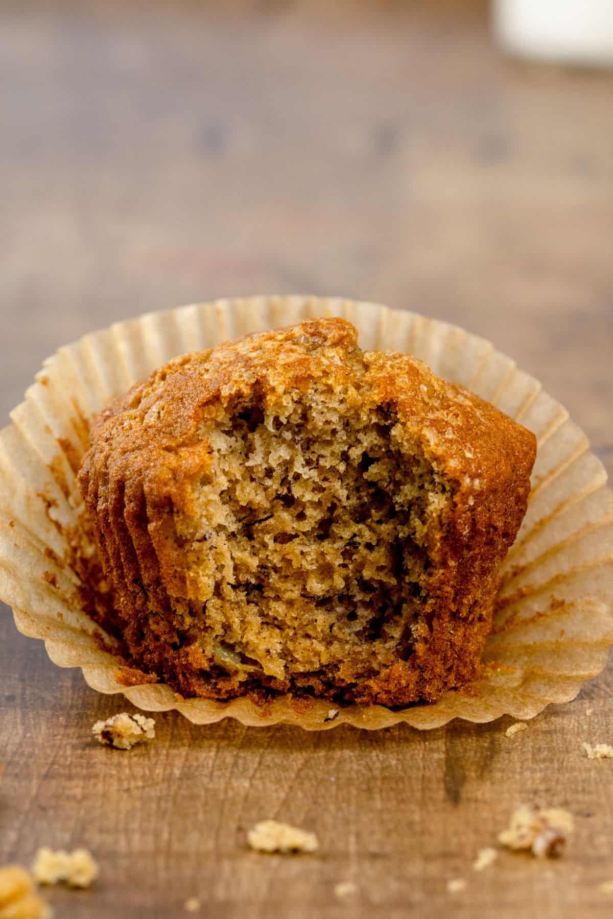 a partially unwrapped gluten free banana muffin with a bite taken out of it so you can see the fluffy inside texture of the muffin