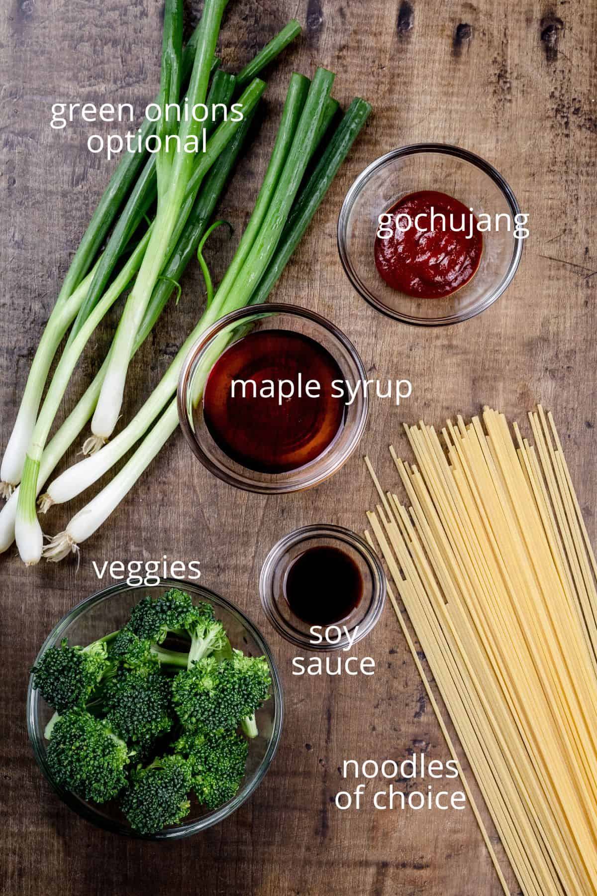 ingredients for gochujang noodles in various glass bowls on a wood table top