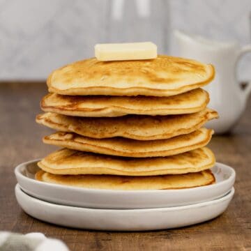 up close stack of egg free pancakes on white round plates with a pat of butter on top of the pancakes.