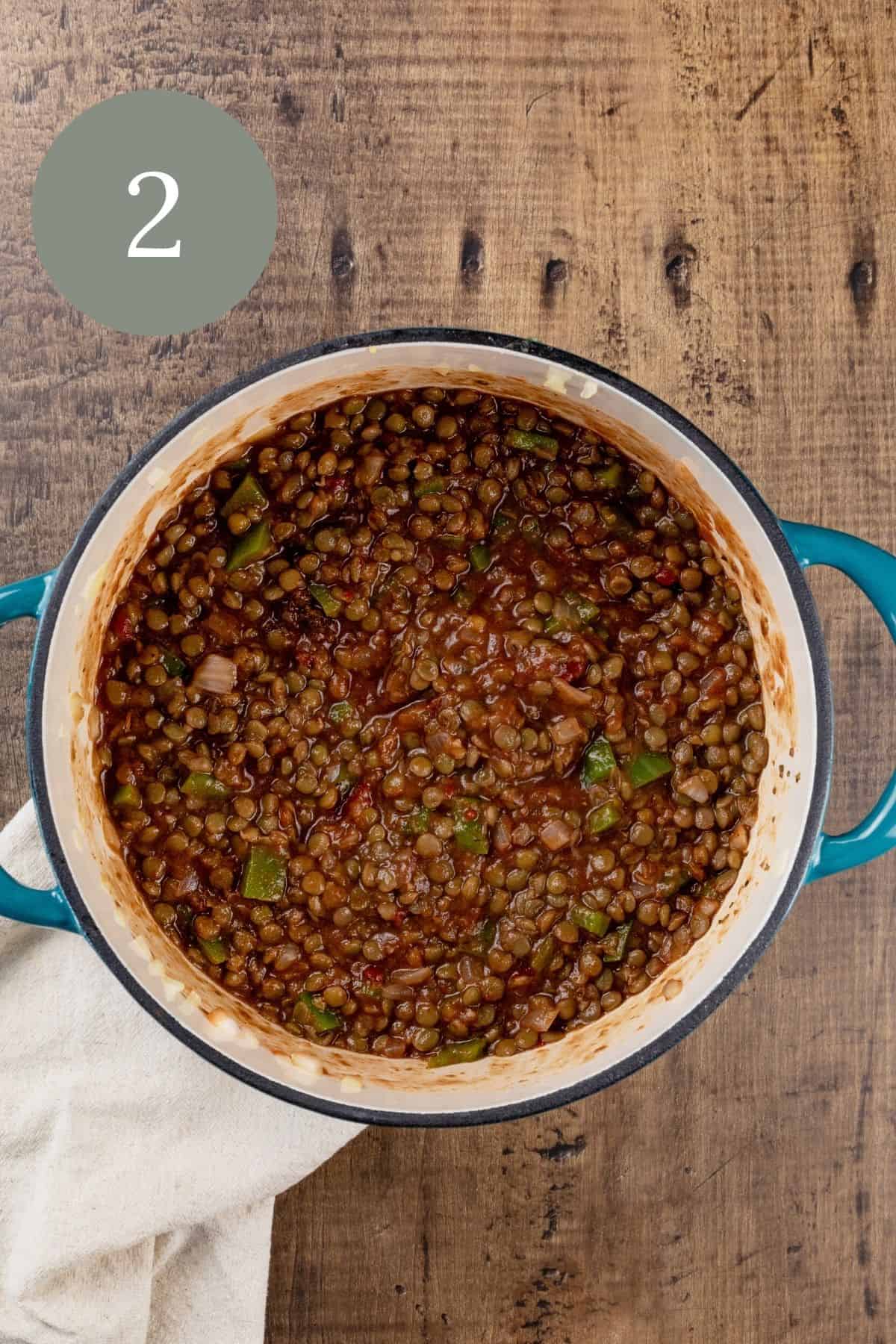 the lentils after adding all the ingredients to the cooking pot. the pot is resting on a linen towel. a green circle with the number 2 is the in the top left corner.