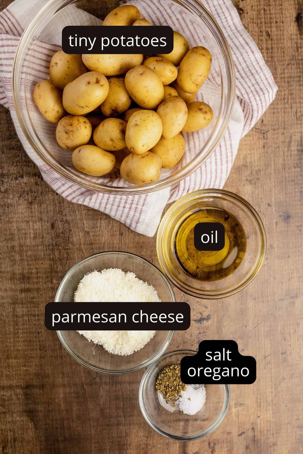 ingredients for parmesan potatoes in various glass bowls on a wood table.