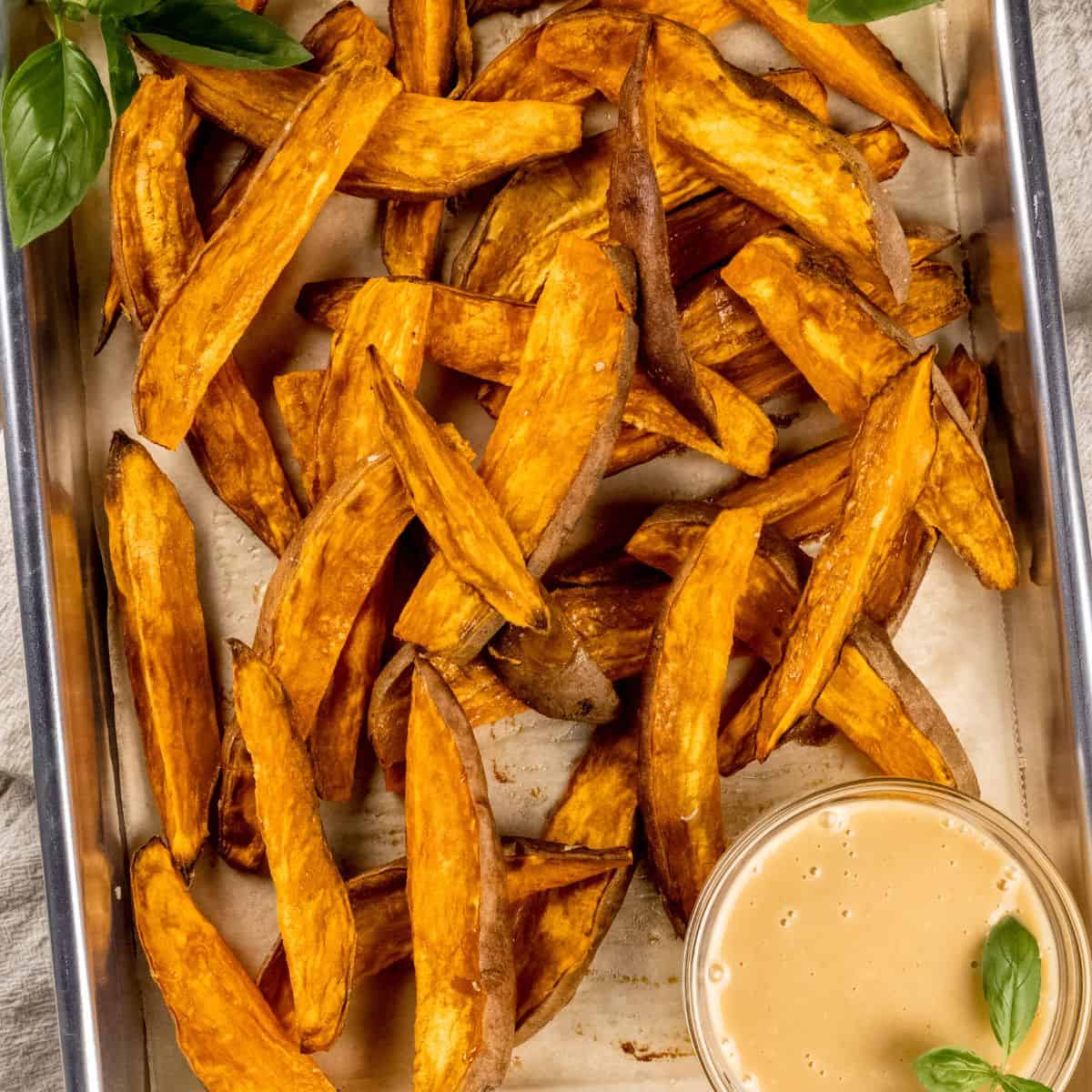 finished sweet potato wedges on a baking sheet with a small bowl of honey mustard dressing in the lower left corner.
