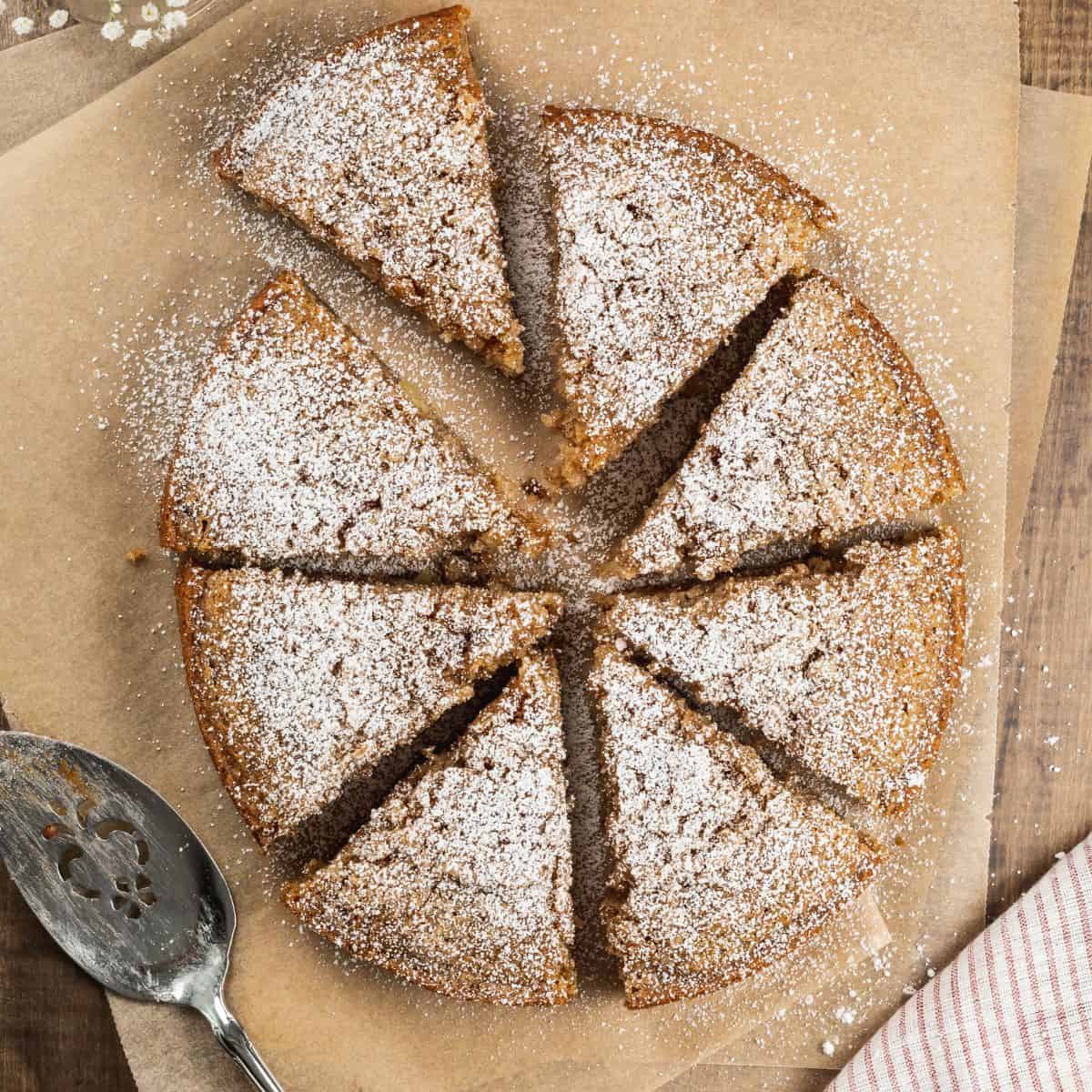 overview of a sliced apple cake cut into triangles and dusted with powdered sugar on brown parchment paper.