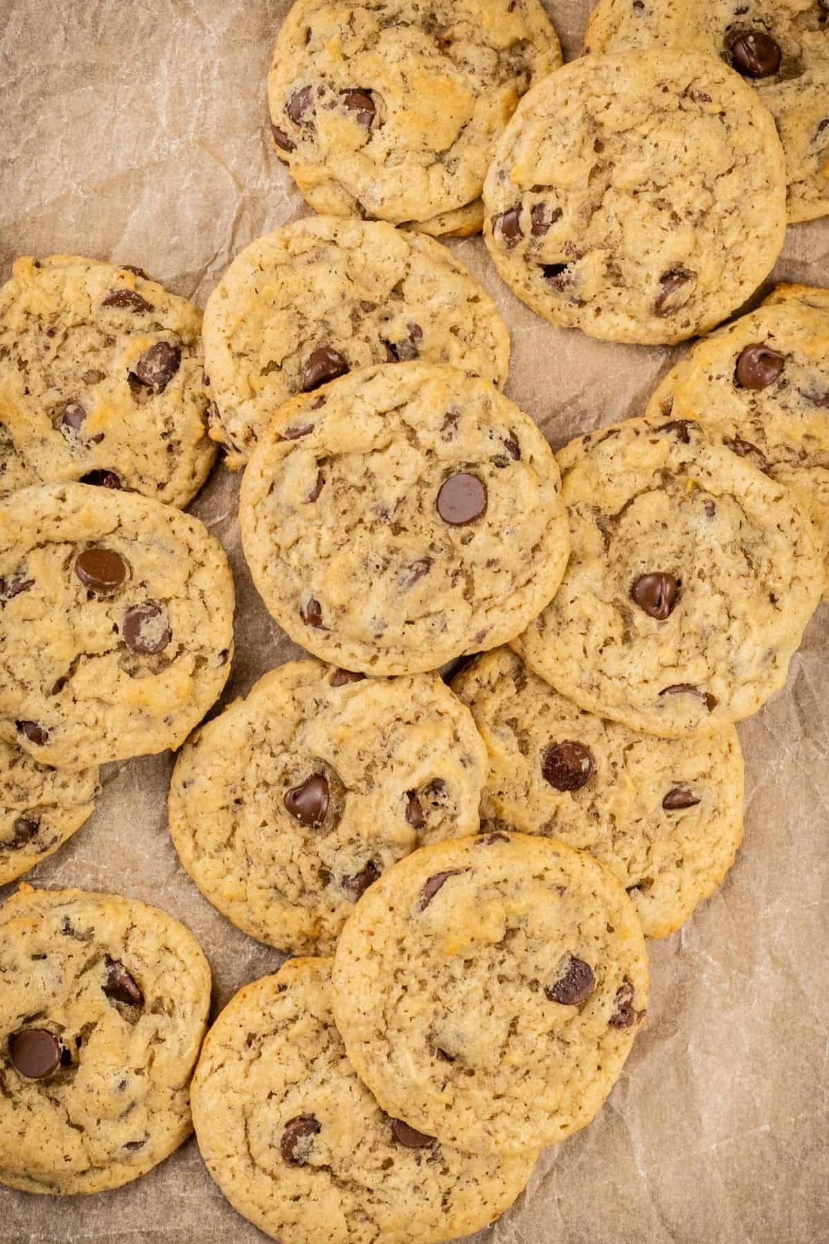 overview of a pile of many layers of vegan banana chocolate chip cookies in a pile on top of brown crinkled parchment paper.
