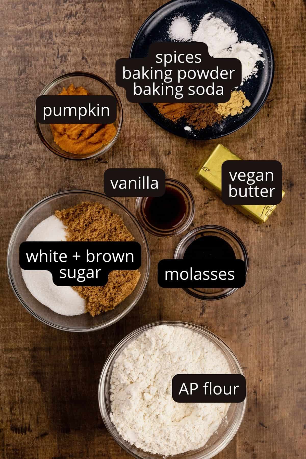 ingredients for pumpkin bars in various glass bowls on a wood table. there are black and white labels that have been added after to label each ingredient.