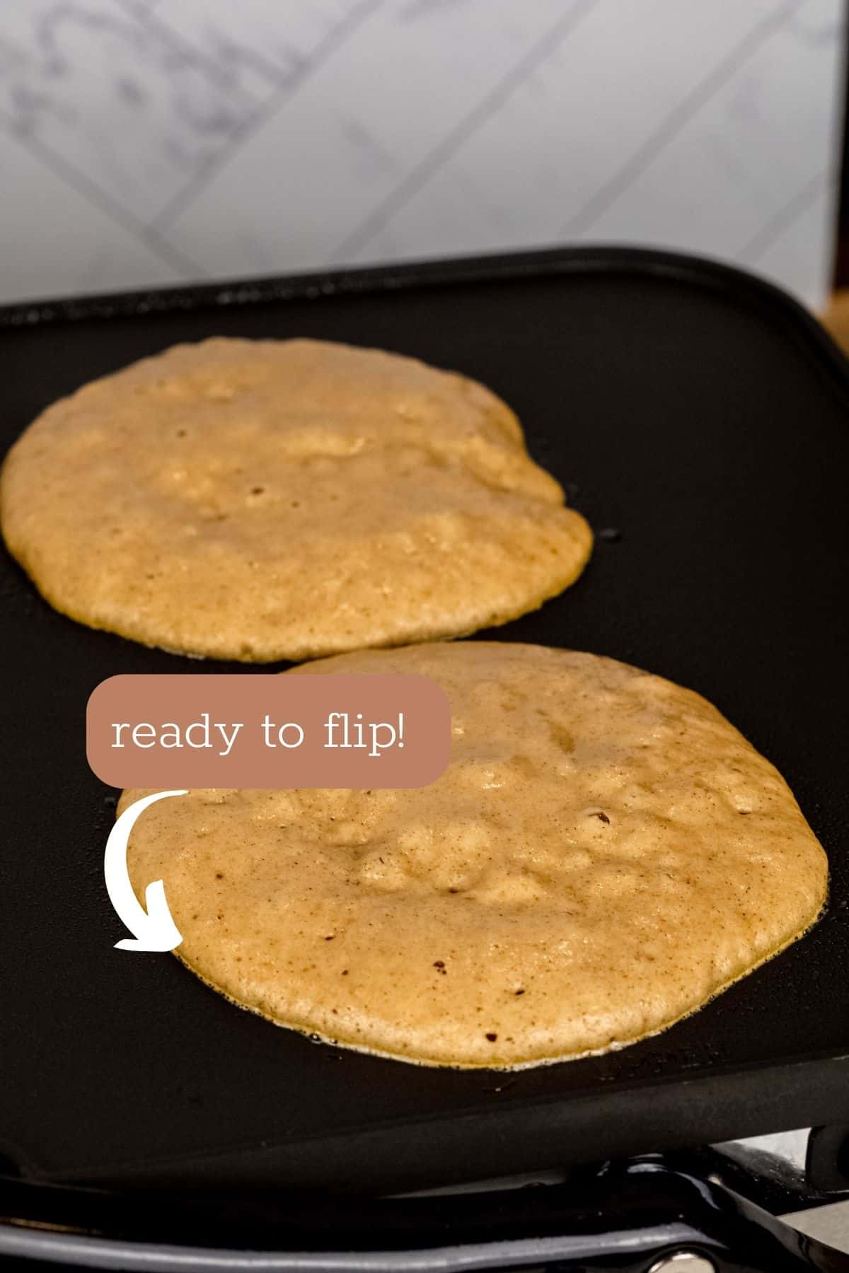 two pancakes on the griddle top ready to flip over.