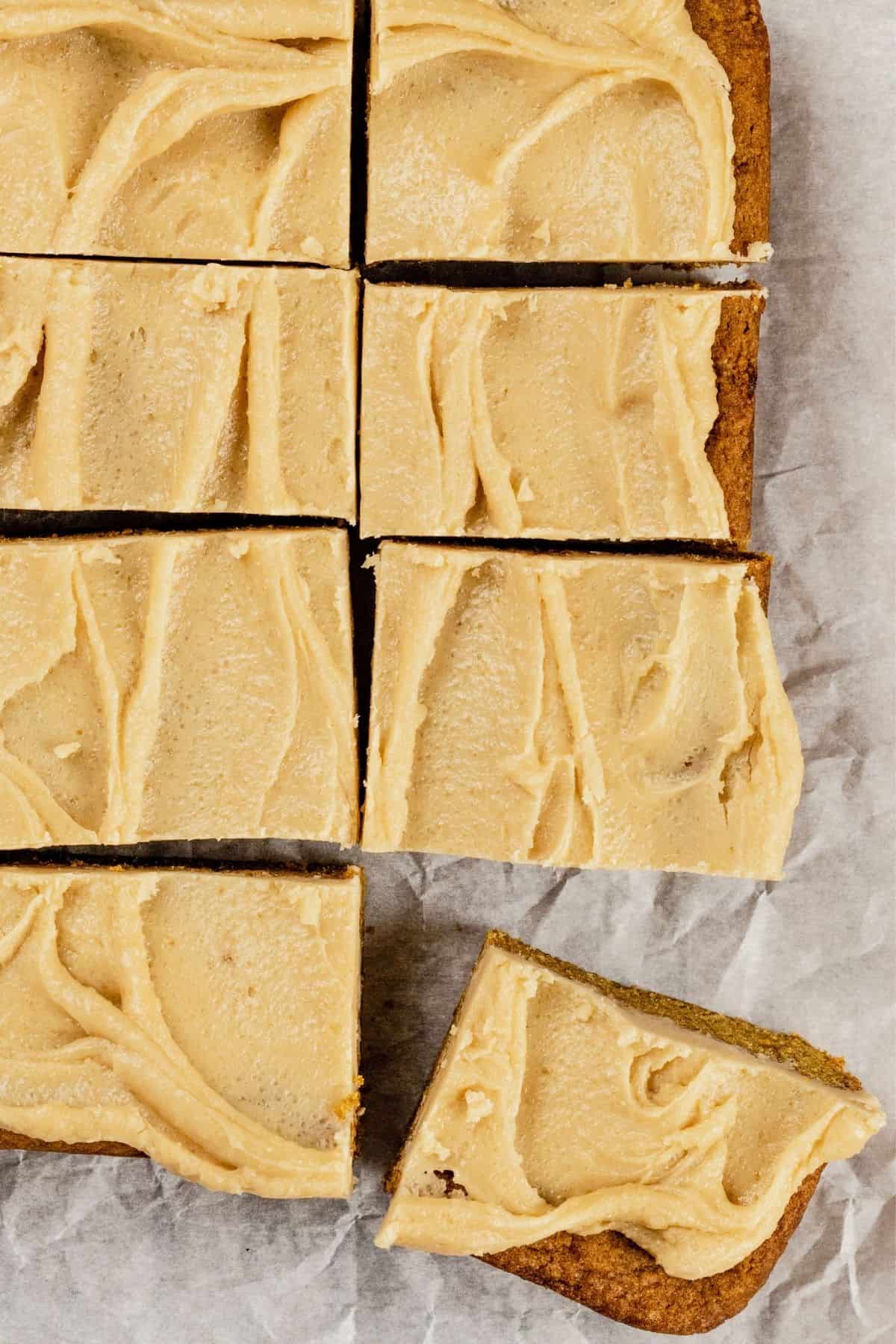 looking down at many slices of pumpkin bars on crinkled white parchment paper. a corner piece is breaking away from the rest of the group.