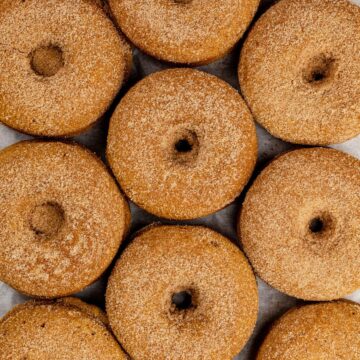 looking at rows of pumpkin donuts covered in cinnamon sugar. a bit of white parchment paper can be seen.