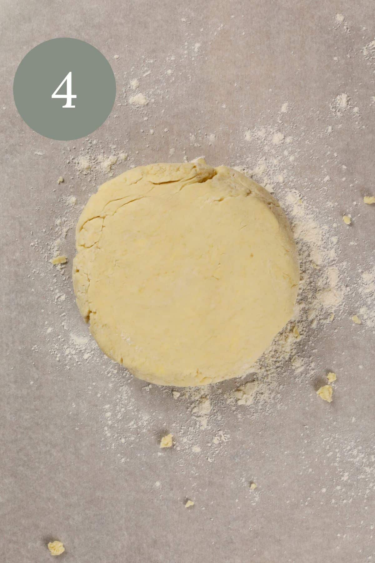 a disc of pie dough on parchment paper with extra flour surrounding it. the number 4 is in the top left corner.