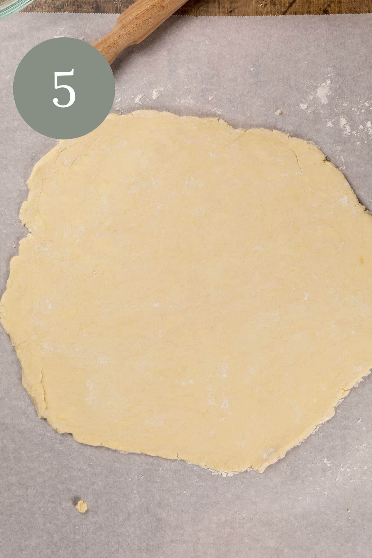 a smooth rolled out gluten free pie crust on a sheet of parchment paper. the rolling pin is just seen in the top edges. the number 5 is in the top left corner.