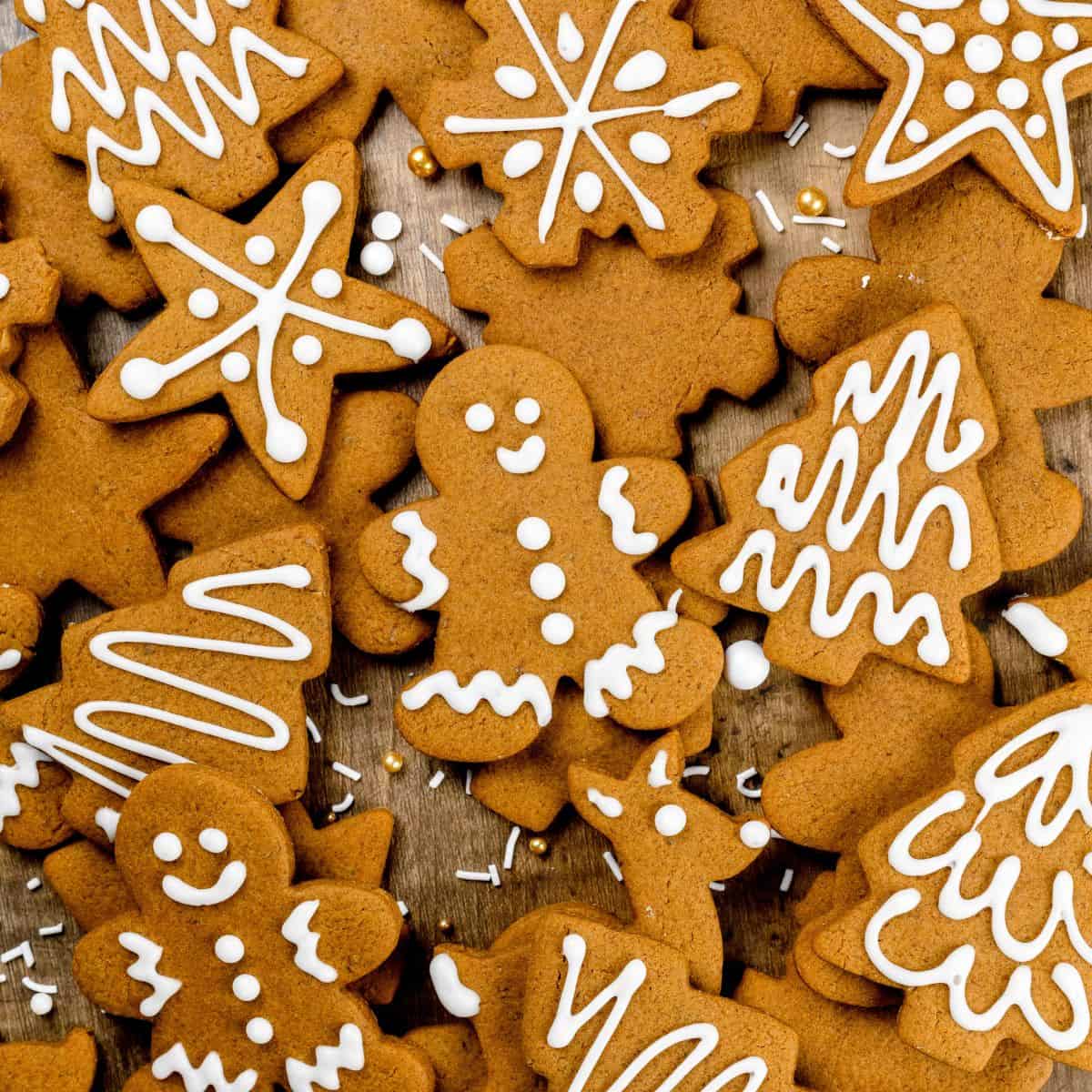 looking at a pile of frosted and unfrosted vegan gingerbread cookies in various shapes like men, trees, and stars. a few sprinkles can be seen. there is white frosting on some of the cookies.