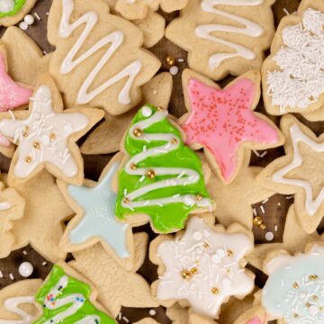 close up of Christmas sugar cookies in various cut out shapes like trees and stars. some have pastel frosting on top with sprinkles. some are plain.