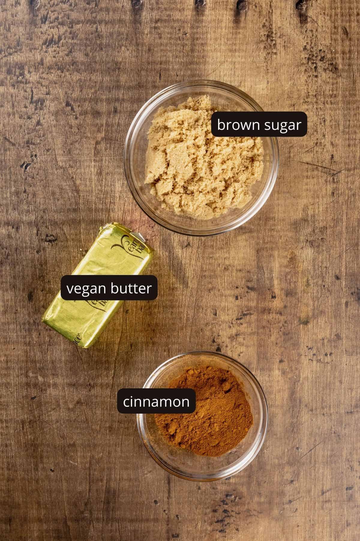 ingredients for the cinnamon filling in glass bowls on a wood tabletop. black and white labels have been added to name each ingredient.