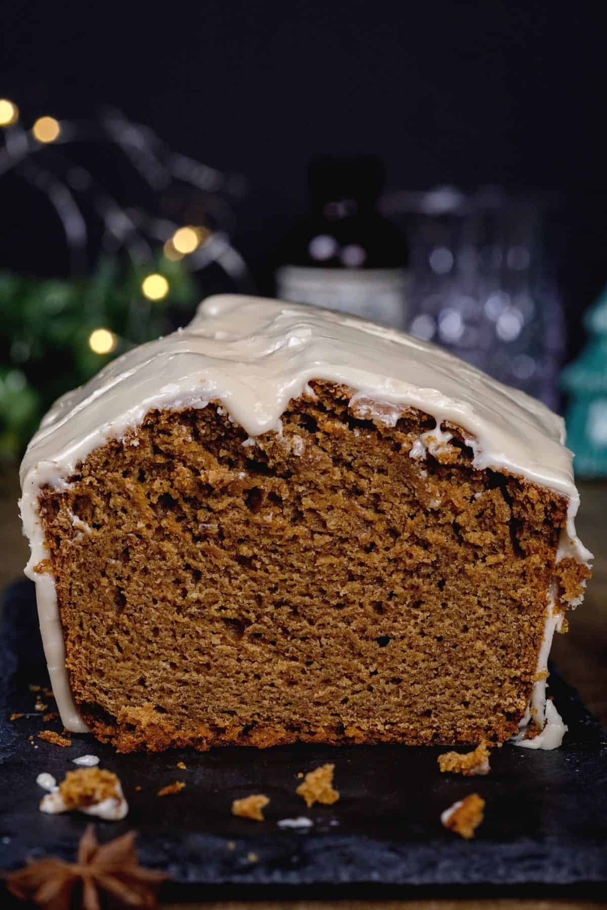 close up of a slice of gingerbread loaf cake so you can see the fully cooked texture. crumbs are in front of the cake. lights are blurred in the background.