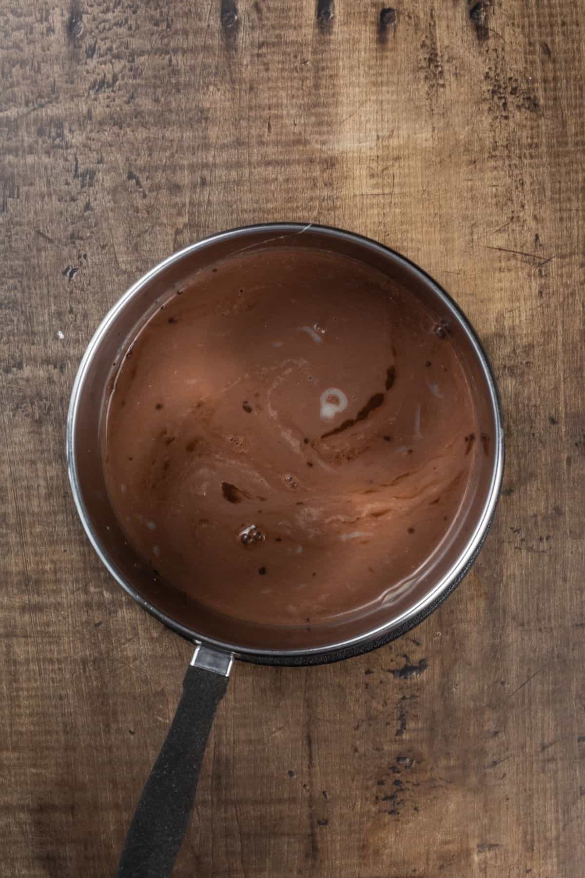 Chocolate pie filling before cooking in a silver pot on a wood table.