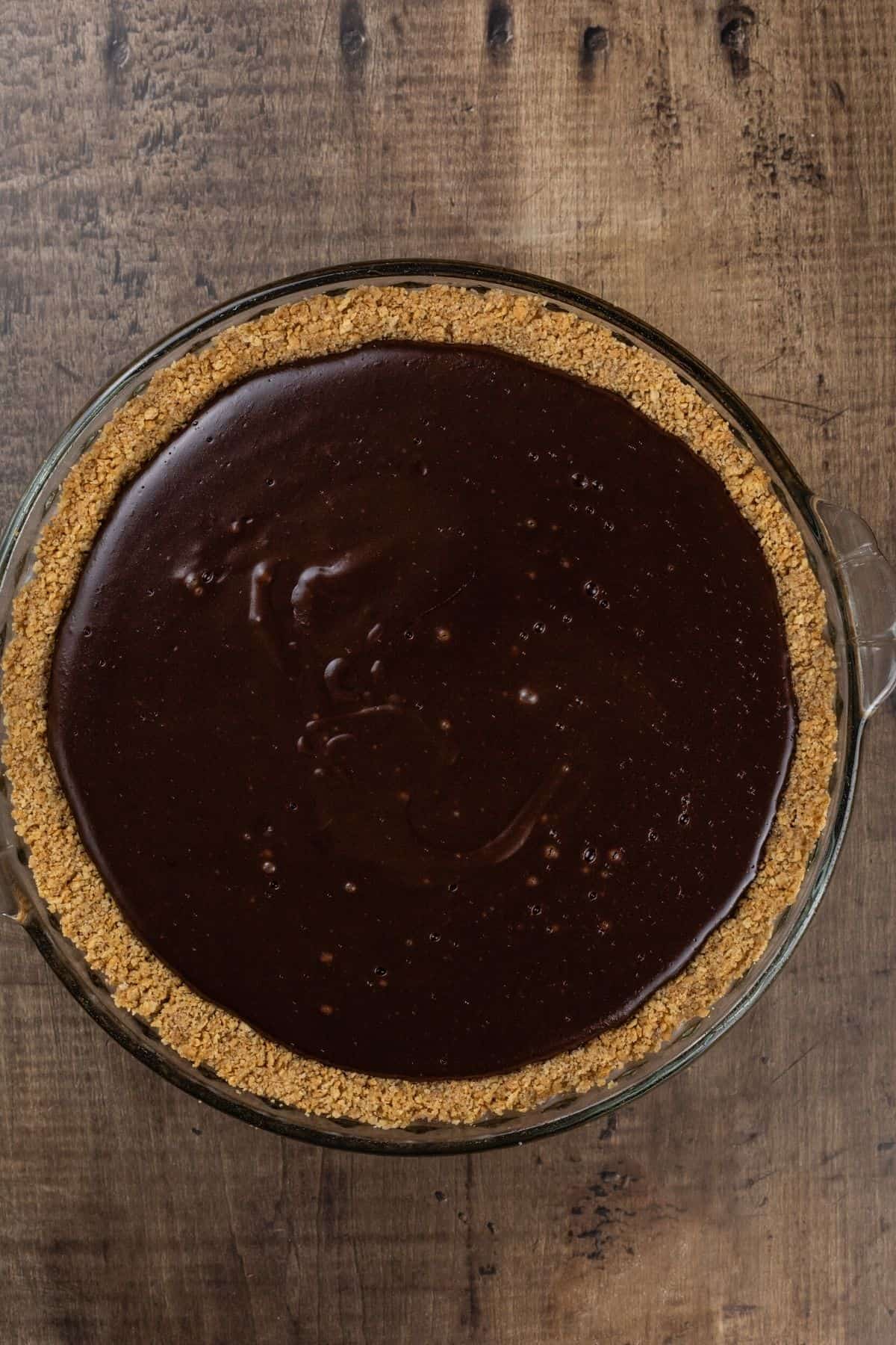 Chocolate pie in a graham cracker crust in a glass pie pan on a wood table.