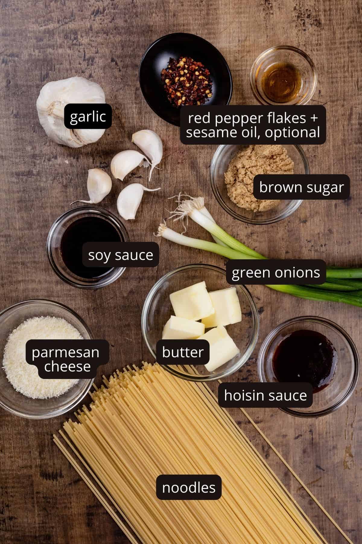Ingredients for garlic butter noodles in various glass bowls on a wood table top. Black and white labels have been added to name each ingredient.