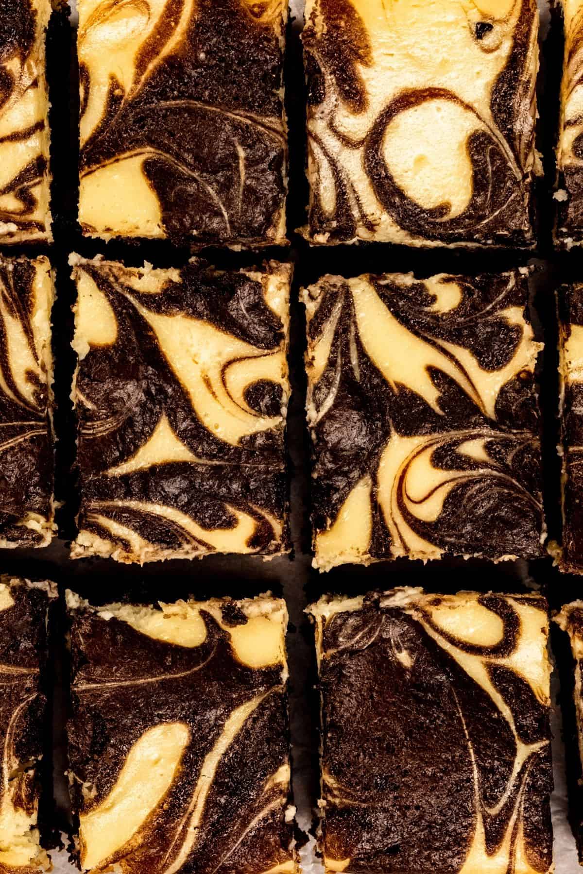 Looking down at cheesecake brownies up close. You can see them sliced into rectangles and the cheesecake and brownie batter have been swirled together on top to look pretty.