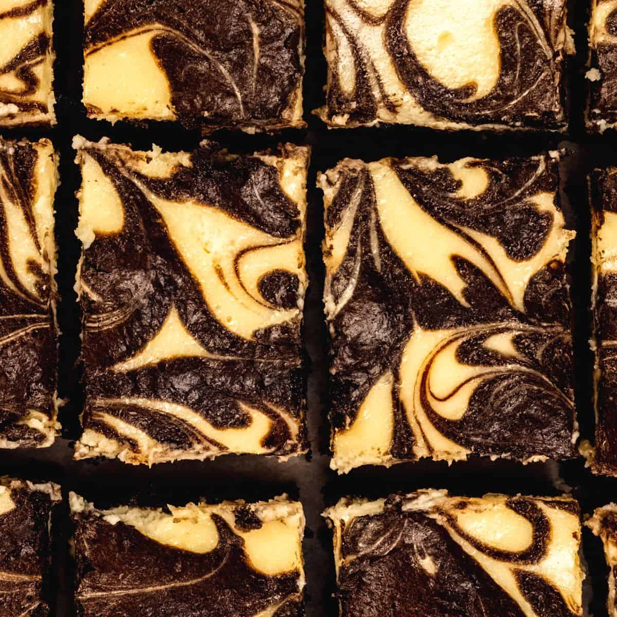 Looking down on an up close view of gluten free cheesecake brownies that have been cut into rectangles. The cheesecake and brownie batter have swirled together.