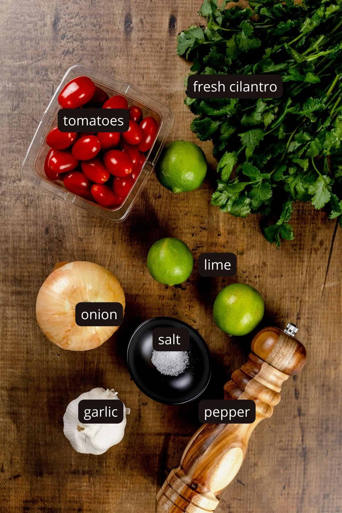 Ingredients for pico de Gallo on a wood tabletop. Black and white labels have been added to name each ingredient.