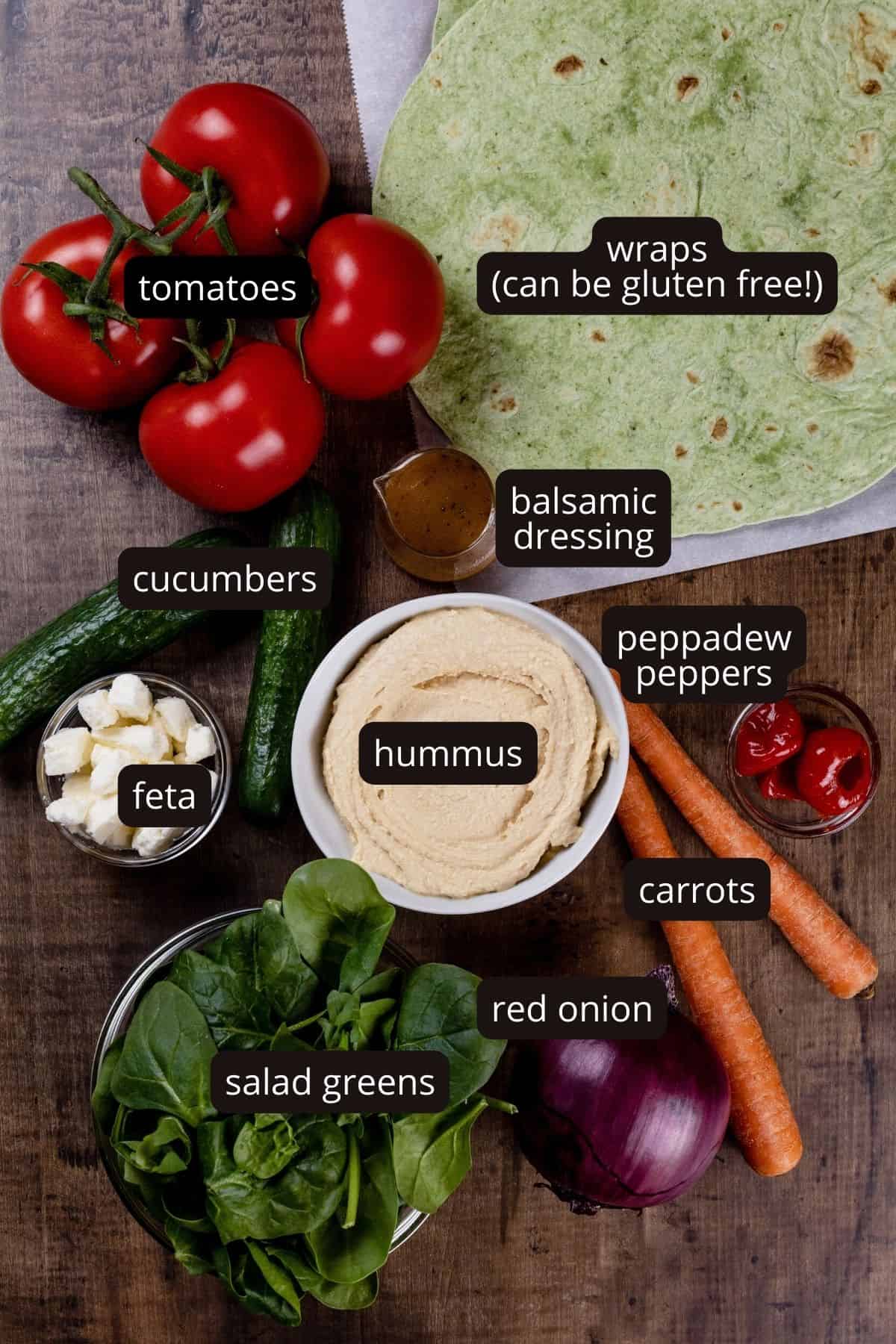 Ingredients for the veggie wrap in various glass bowls on a wood tabletop. Black and white labels have been added to name each ingredient.