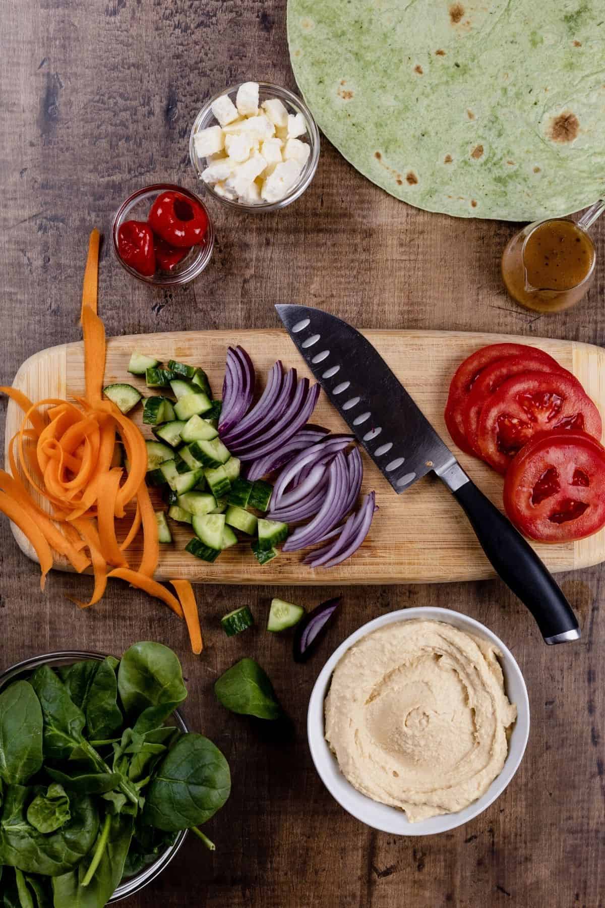 A wood cutting board with a knife cutting and slicing veggies for the wrap sandwich.