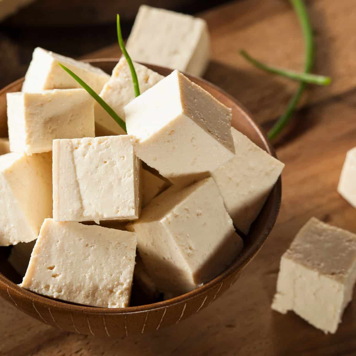 A wood bowl is filled with large cubes of raw tofu.