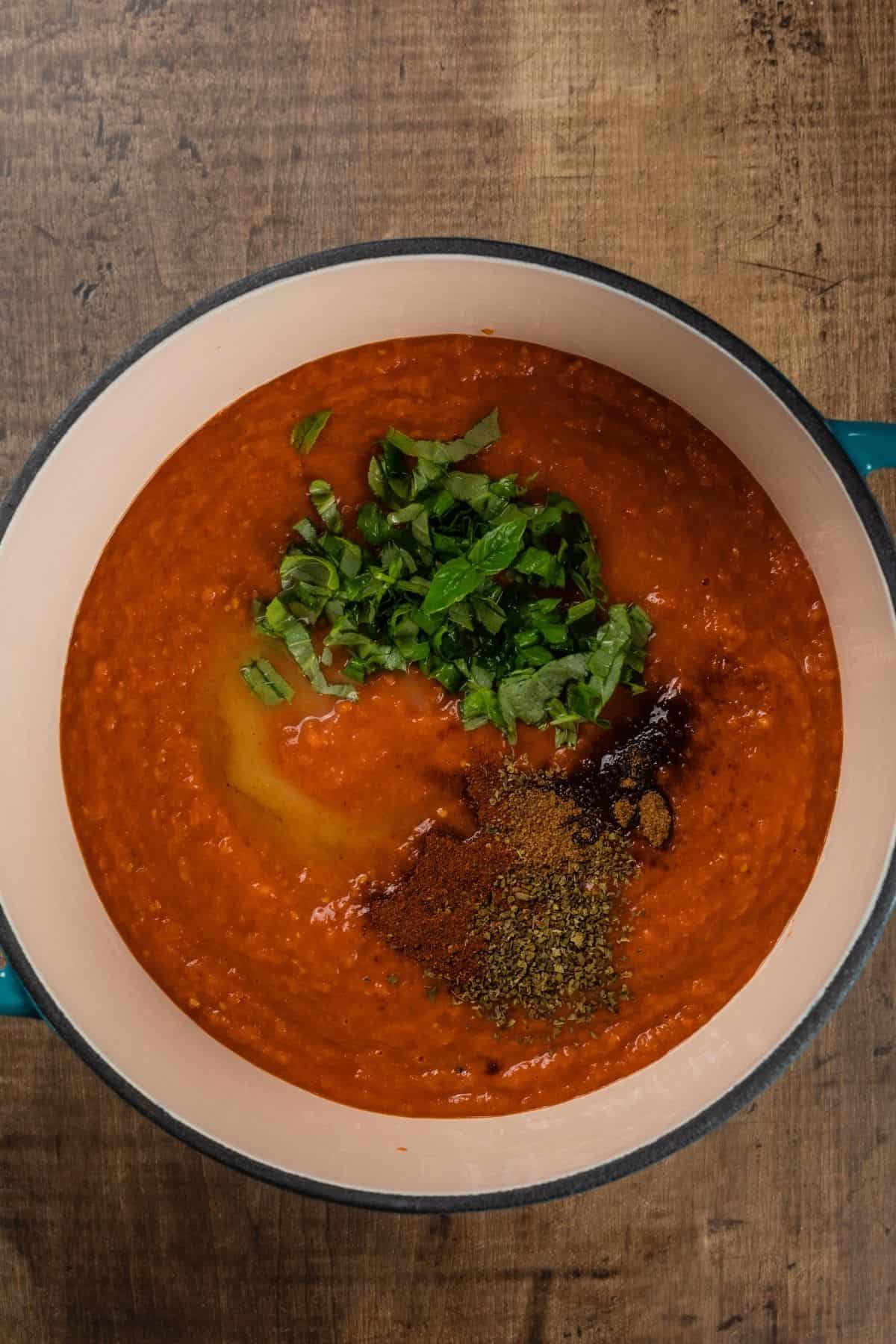 A large ceramic cooking pot is filled with the tomato soup and the fresh herbs and spices have been added on top before cooking.