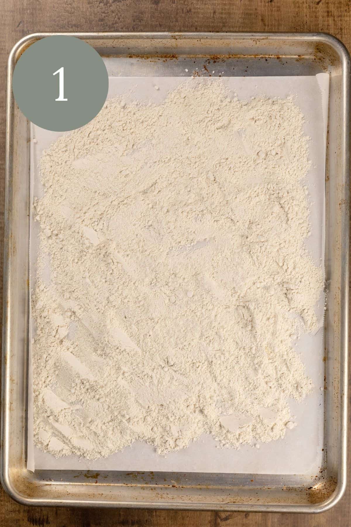 A silver baking tray lined with white parchment paper is covered in wheat flour. A green circle with the number 1 is in the top left corner.