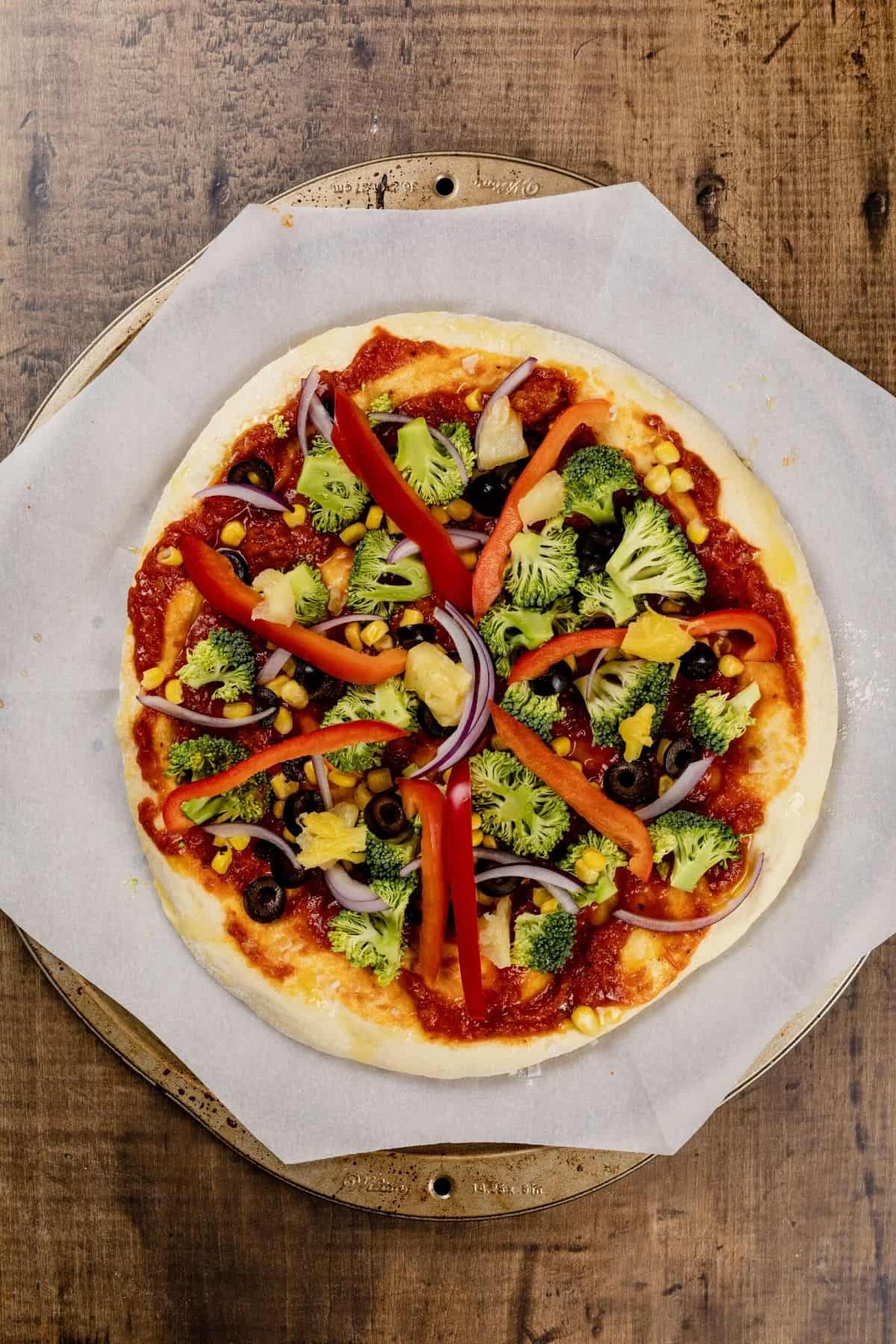 A broccoli and red pepper vegan pizza before baking on a metal pizza tray.