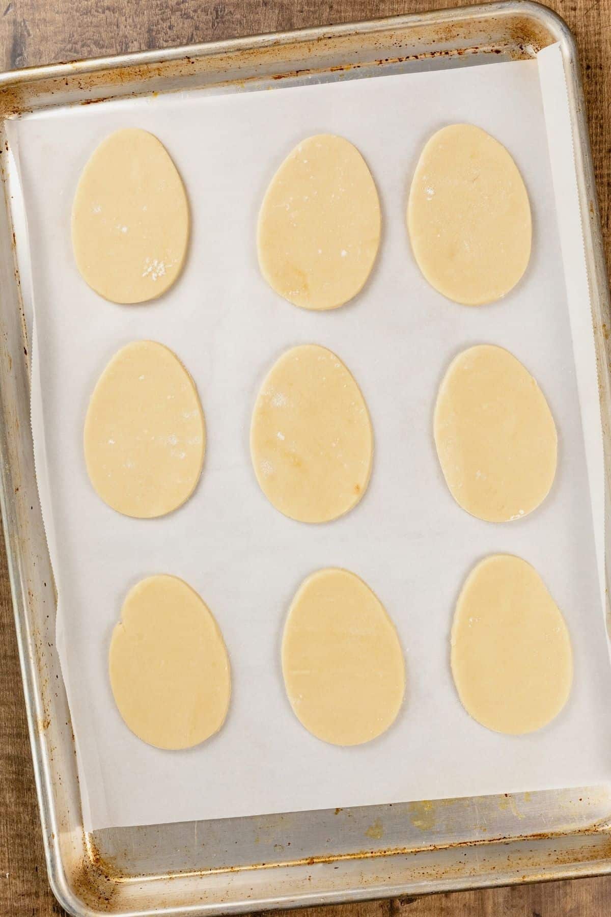 A silver cookie tray with parchment paper and 9 unbaked cookies.