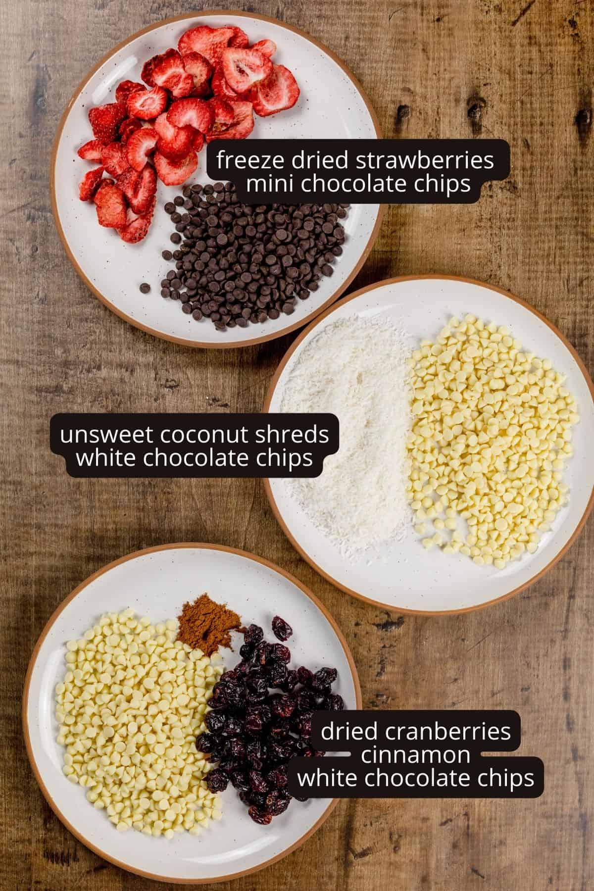 3 beige plates are on a wood table top. Each plate is filled with various mix-ins for the cookies. Strawberries, coconut, and cranberries are some of in the ingredients. Black and white labels have been added to name each ingredient.