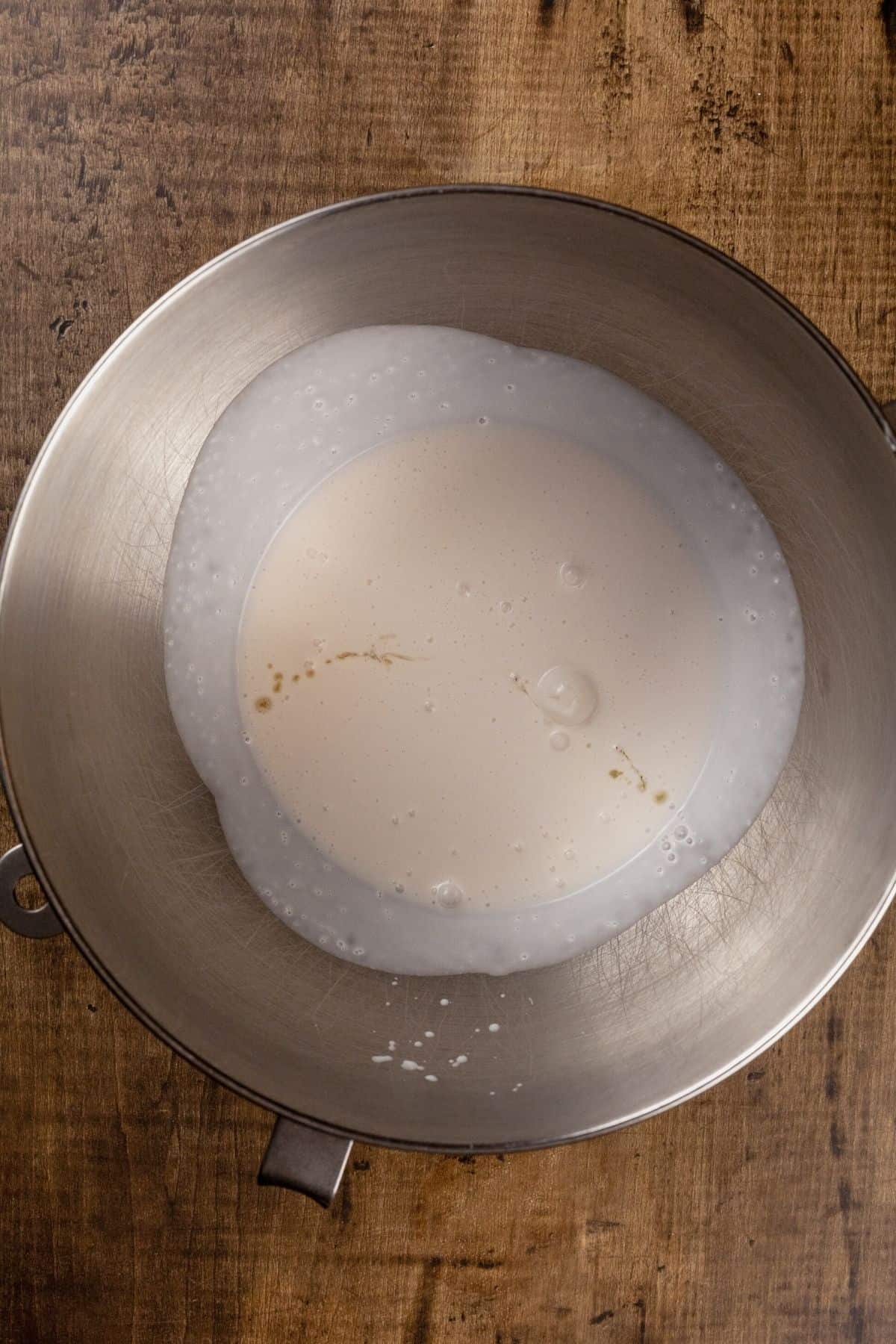 The wet ingredients in a silver mixing bowl on a wood tabletop.
