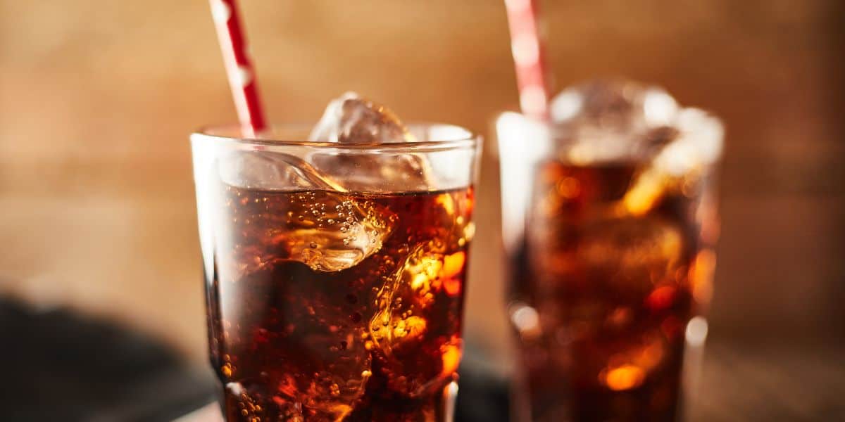 A close up of a glass filled with soda pop with a red straw. A second glass is blurred in the background.