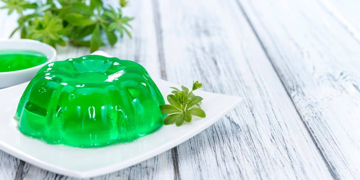 Green jello in a bundt shape on a white plate with greenery next to it.