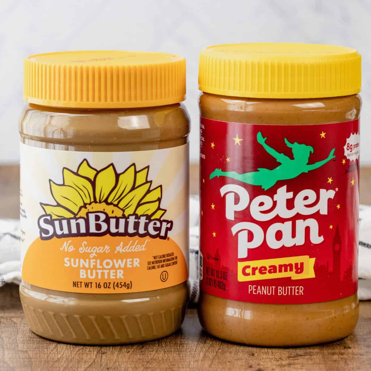 A jar of SunButter next to a jar of Peanut Butter on the wood tabletop in the kitchen.