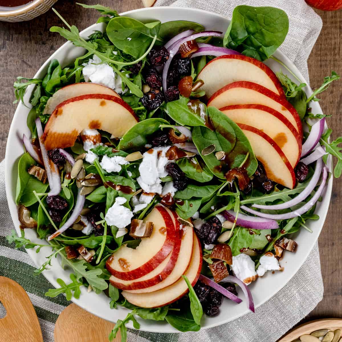 A big bowl filled with a fuji apple salad with apple slices, red onion, feta cheese, and balsamic dressing.
