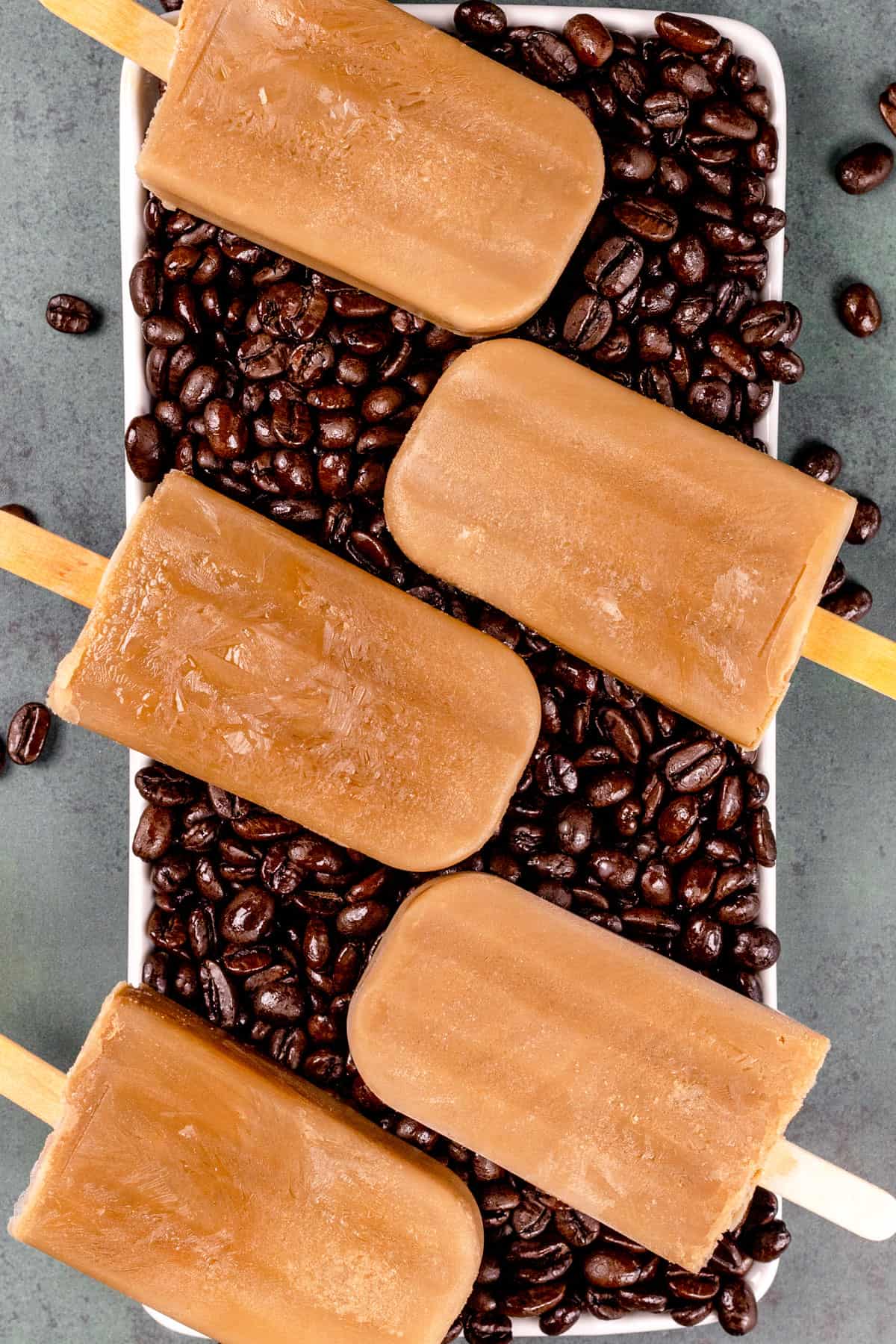 5 coffee popsicles on a long white serving tray filled with roasted coffee beans.