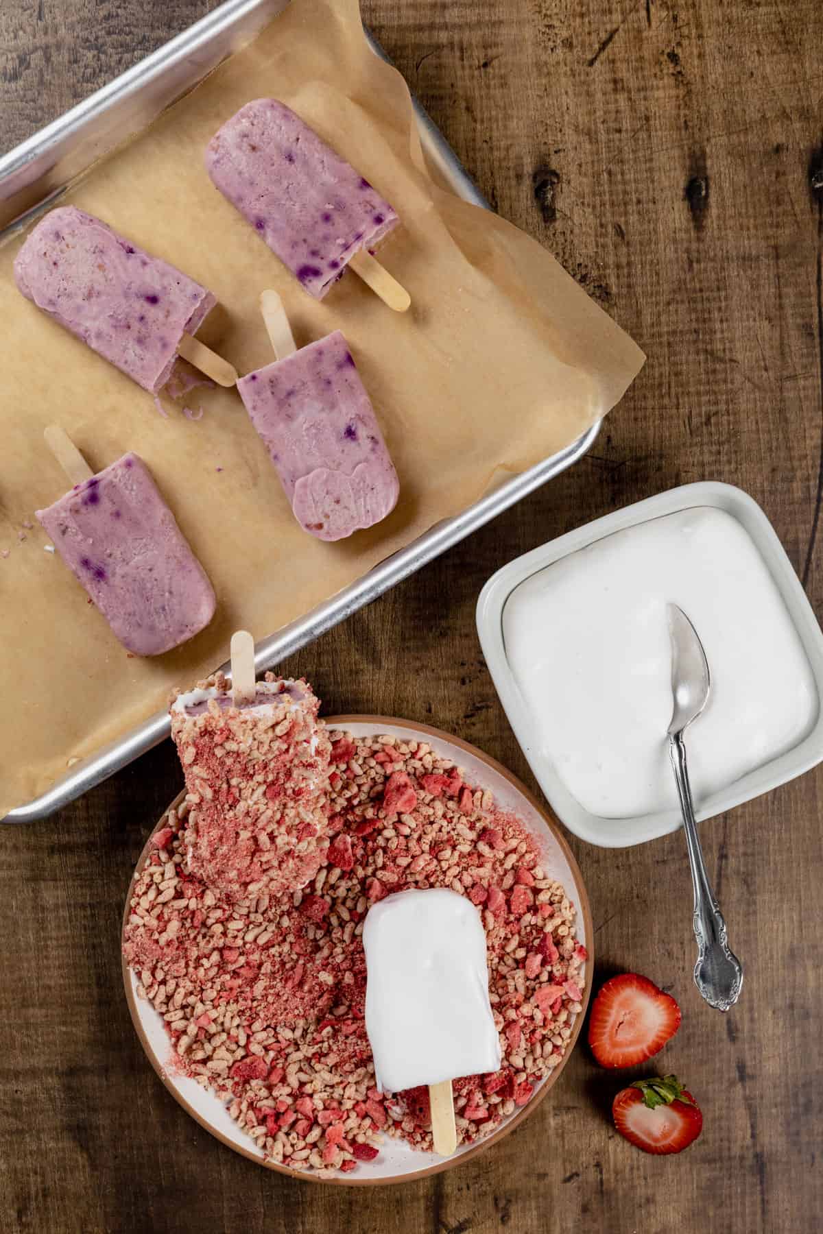 A plate filled with the strawberry crumb mixture, a bowl filled with dairy free whipped cream, and a tray filled with the strawberry shortcake ice cream bars.