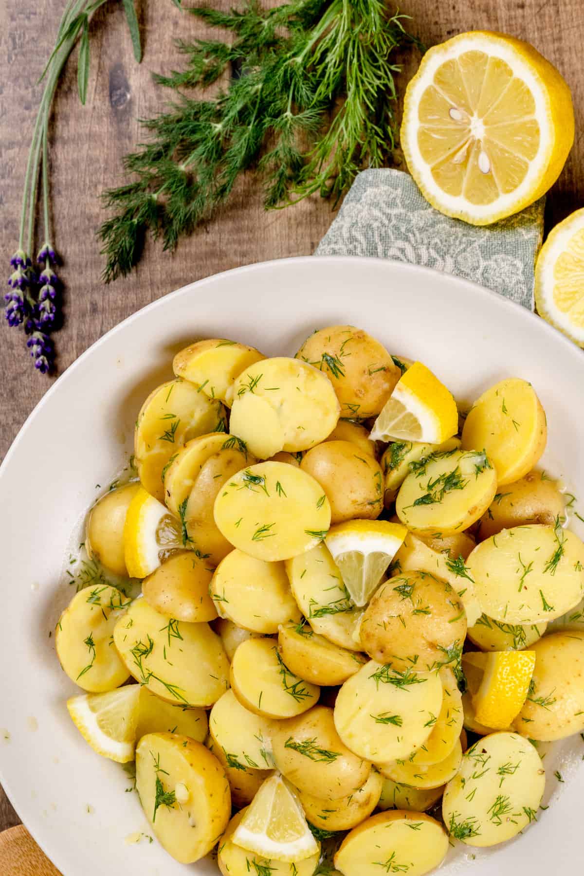 Closeup of a beige bowl filled with potato salad made without eggs. Fresh lemon wedges and slices are in and next to the bowl as well as fresh dill.