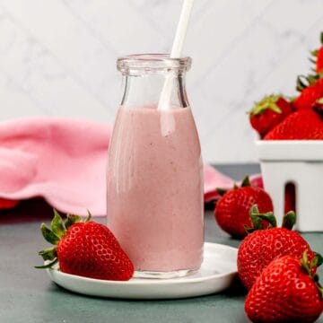 Strawberry milk in a glass jar with a white straw. Fresh berries surround the glass.