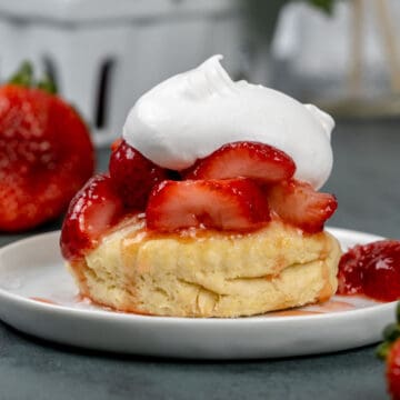 A finished vegan strawberry shortcake on a white plate with a dollop of whipped cream on top. Fresh berries surround the plate.