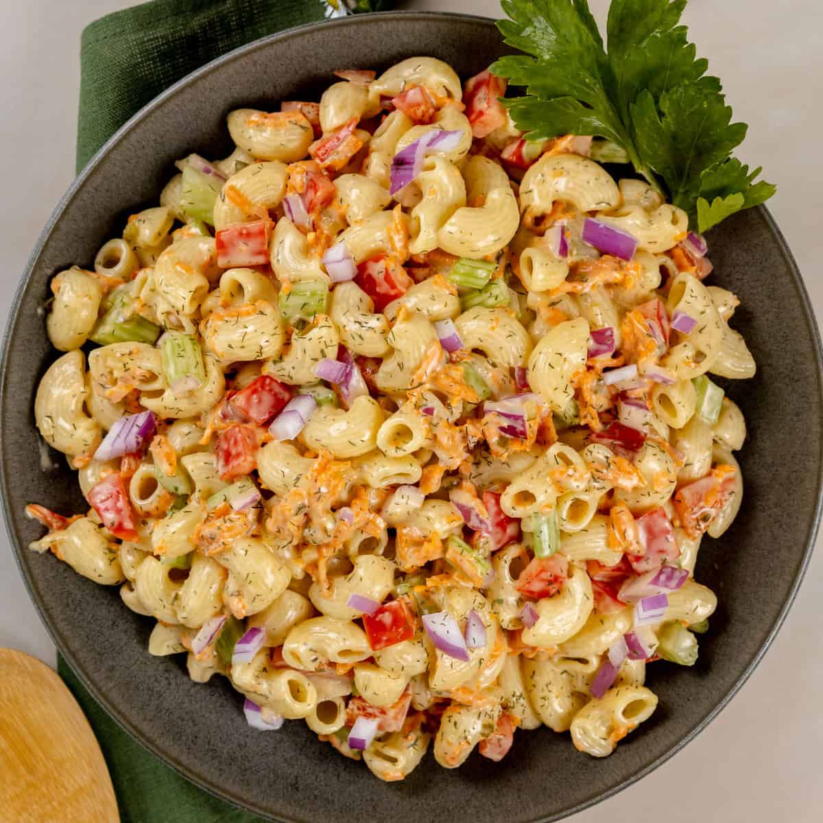 A dark big bowl filled with vegan macaroni salad with creamy dressing. It is resting on a green napkin.