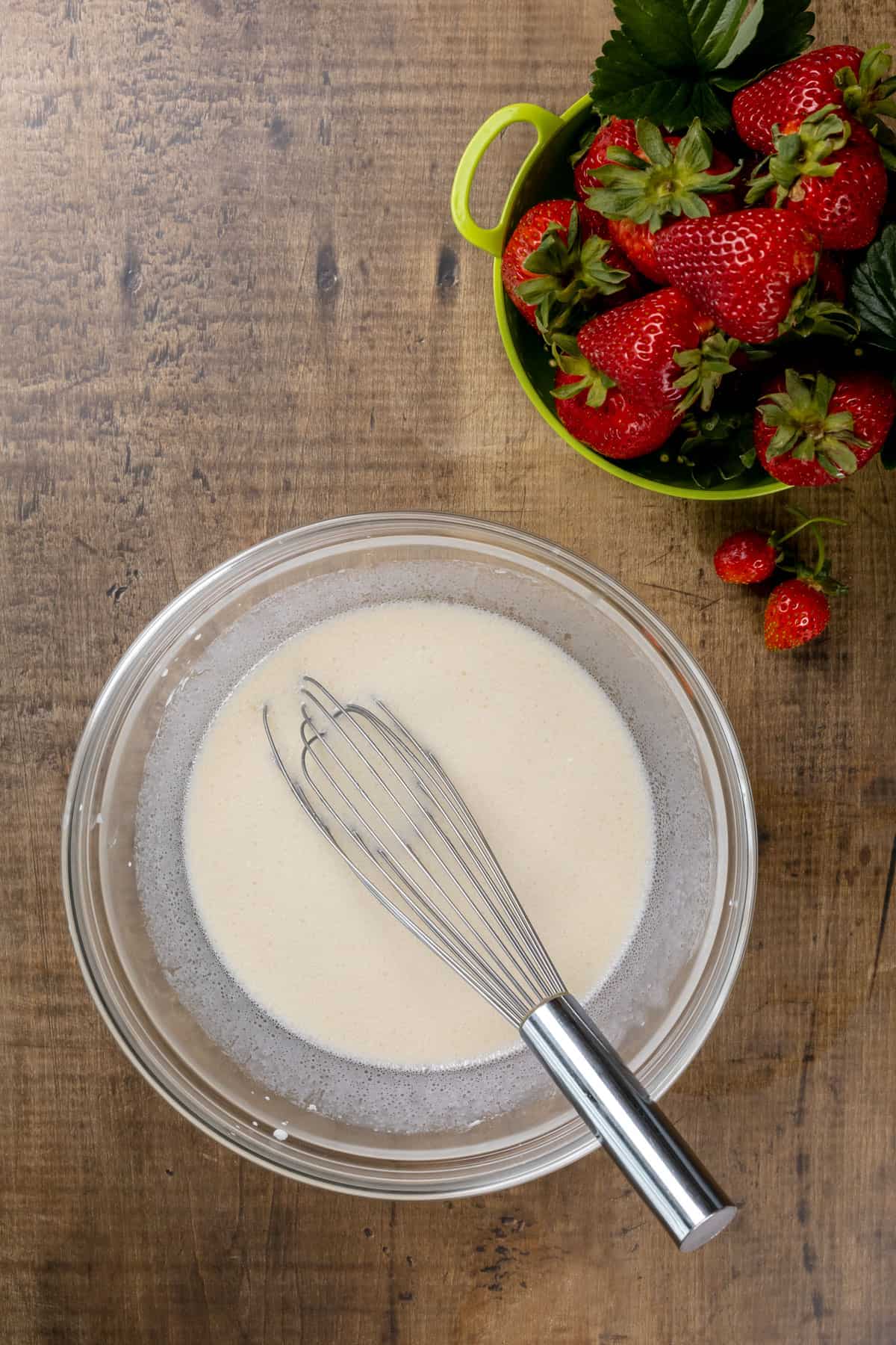A glass bowl is filled with the wet ingredients for the shortcakes. A bowl of fresh strawberries are next to the bowl.
