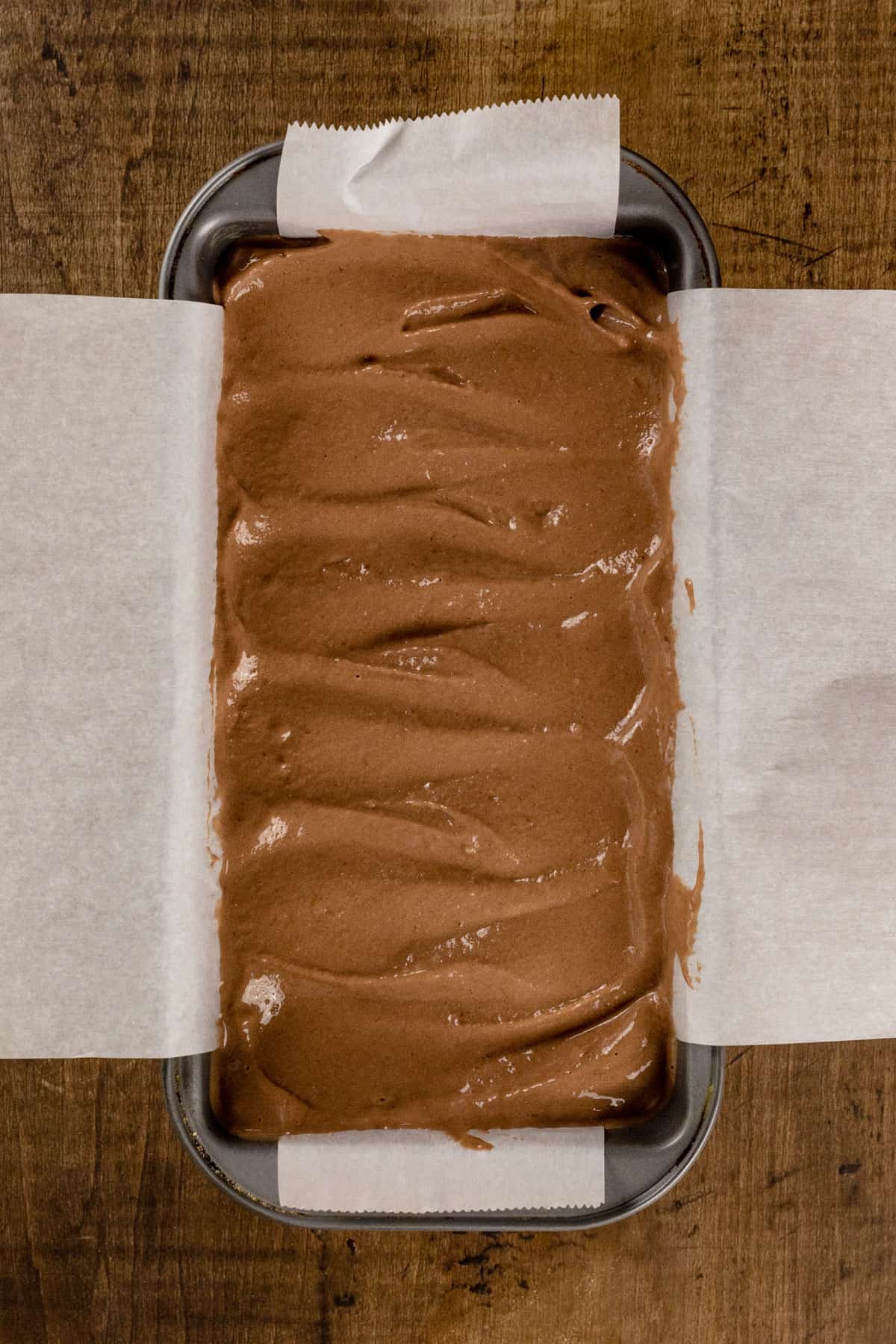 Chocolate nice cream in a loaf pan lined with parchment paper.