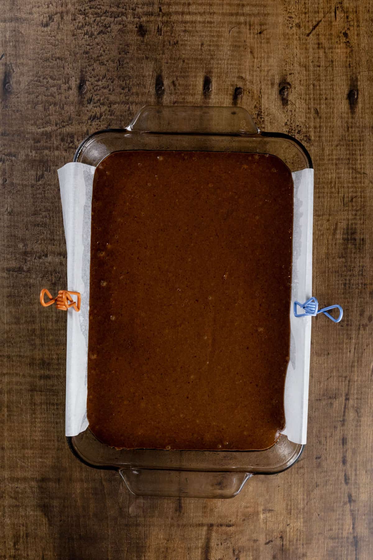 The chocolate cake in a glass pan with parchment paper before baking.