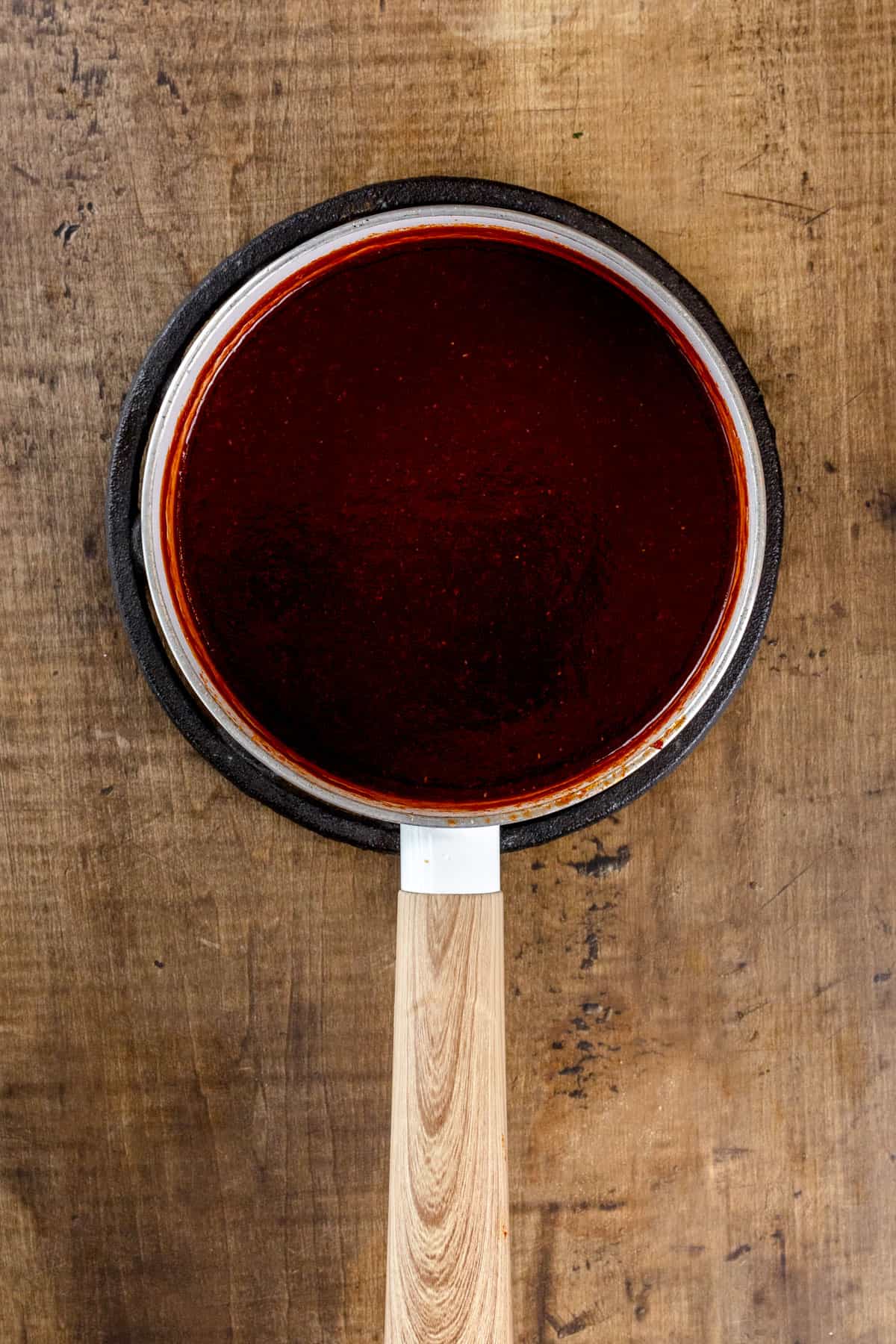 A white pot on a wood kitchen table is filled with bbq sauce after cooking.